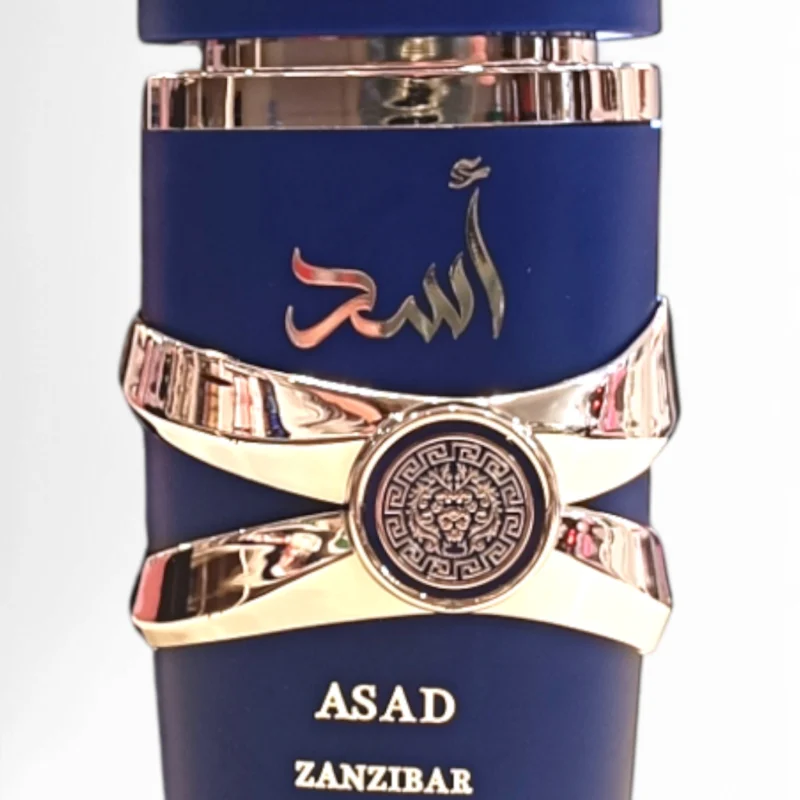 Lattafa Asad Zanzibar EDP 100 ml se presenta en un frasco azul con detalles plateados, escritura árabe y motivos decorativos en la parte frontal, mientras que los nombres de la marca y del producto aparecen en letras doradas.