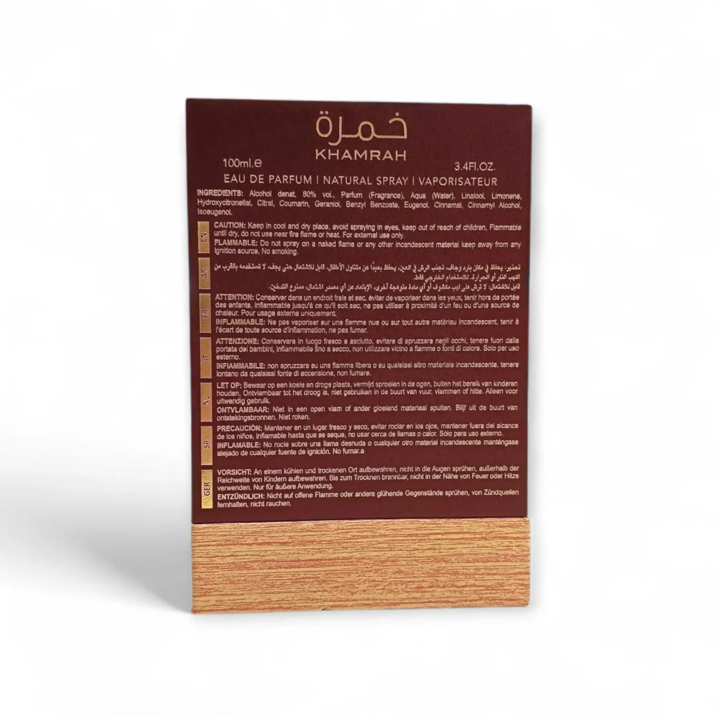 Reverso de una caja de perfume Khamrah, con detalles del producto, ingredientes, advertencias, instrucciones e información del fabricante en inglés y francés, con fondo granate y diseño de vetas de madera en la parte inferior. Reverso de una caja de perfume Khamrah, con detalles del producto, ingredientes, advertencias, instrucciones e información del fabricante en inglés y francés, con fondo granate y diseño de vetas de madera en la parte inferior.