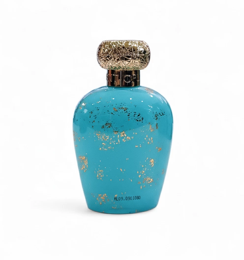 Frasco de perfume turquesa con motas doradas y tapón redondo dorado ornamentado, sobre fondo blanco liso.