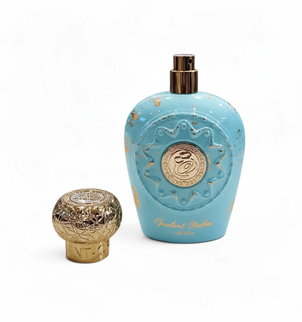 Frasco de perfume turquesa con detalles dorados y un decorativo tapón redondo dorado al lado. El frasco presenta detalles ornamentales y escritura árabe dorada, y lleva la etiqueta "Opulent Dubai Lattafa".