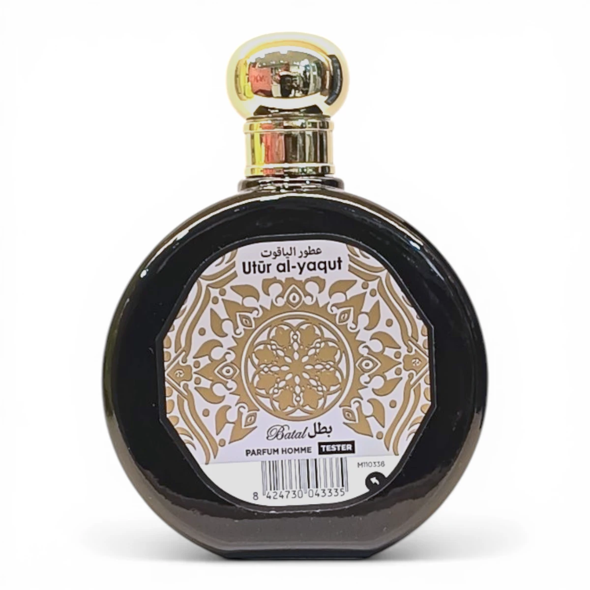 Frasco redondo de vidrio oscuro con tapón dorado. La etiqueta frontal presenta intrincados motivos dorados y blancos, texto en árabe y el nombre Utûr al-yaqut Batal Parfum Homme Tester.