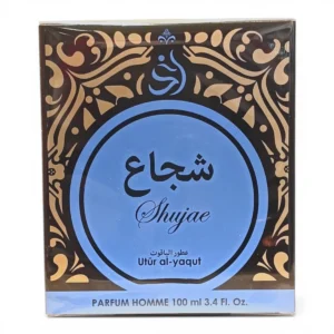 Caja de perfume con motivos ornamentales dorados y negros sobre fondo marrón, en la que figura un gran círculo azul con el texto árabe Shujae y Utür al-yaqut en inglés debajo. La caja lleva la etiqueta PARFUM HOMME 100 ml 3.4 FL. Oz.