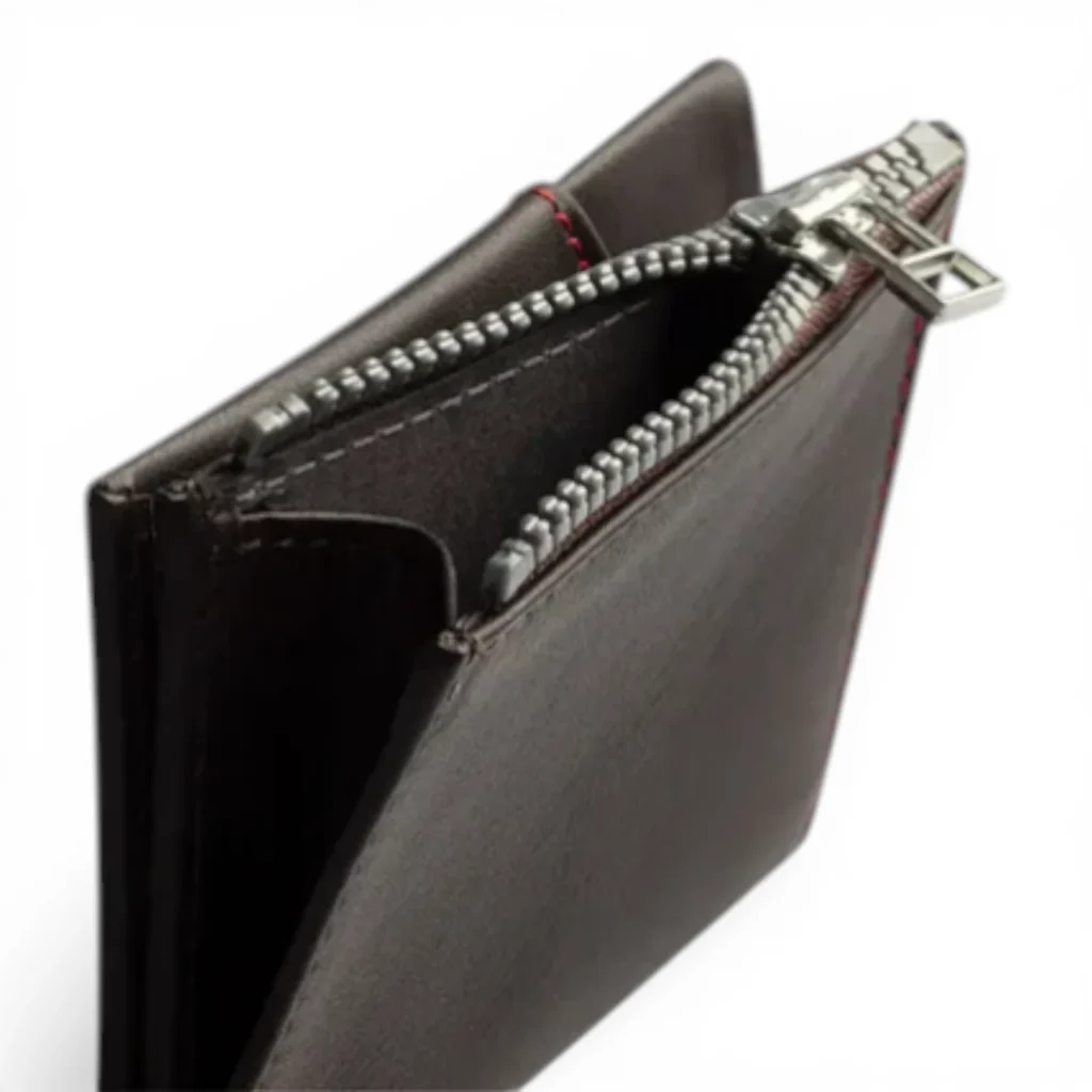 Primer plano de una cartera de cuero marrón oscuro con la cremallera parcialmente abierta, mostrando sus compartimentos interiores y el detalle de las costuras rojas. Primer plano de una cartera de cuero marrón oscuro con la cremallera parcialmente abierta, mostrando sus compartimentos interiores y el detalle de las costuras rojas.