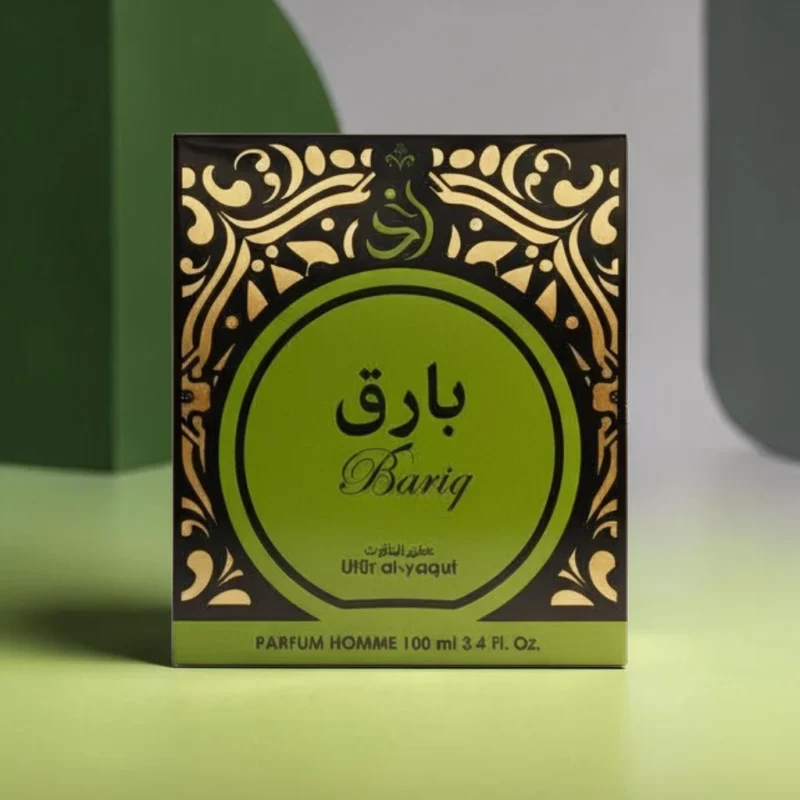 Caja verde y negra de Bariq Parfum Homme con motivos decorativos dorados y texto en árabe e inglés, expuesta sobre una superficie clara con sombras geométricas de fondo.