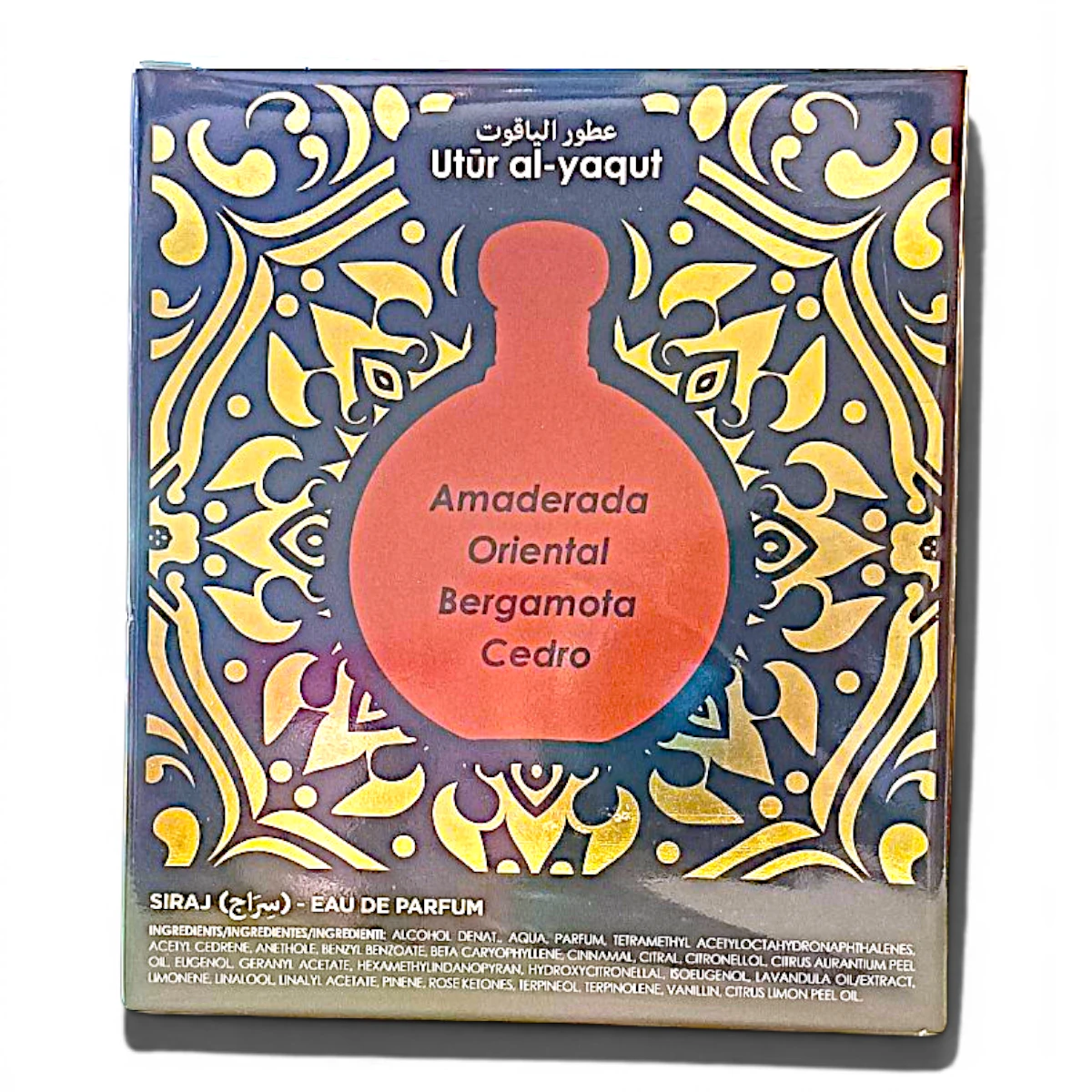 Una caja de perfume decorativa con un motivo ornamental dorado y azul, con la silueta de un frasco rojo en el centro que muestra las notas de la fragancia: Amaderada, Oriental, Bergamota, Cedro. En la etiqueta se lee Utr al-yaqut.