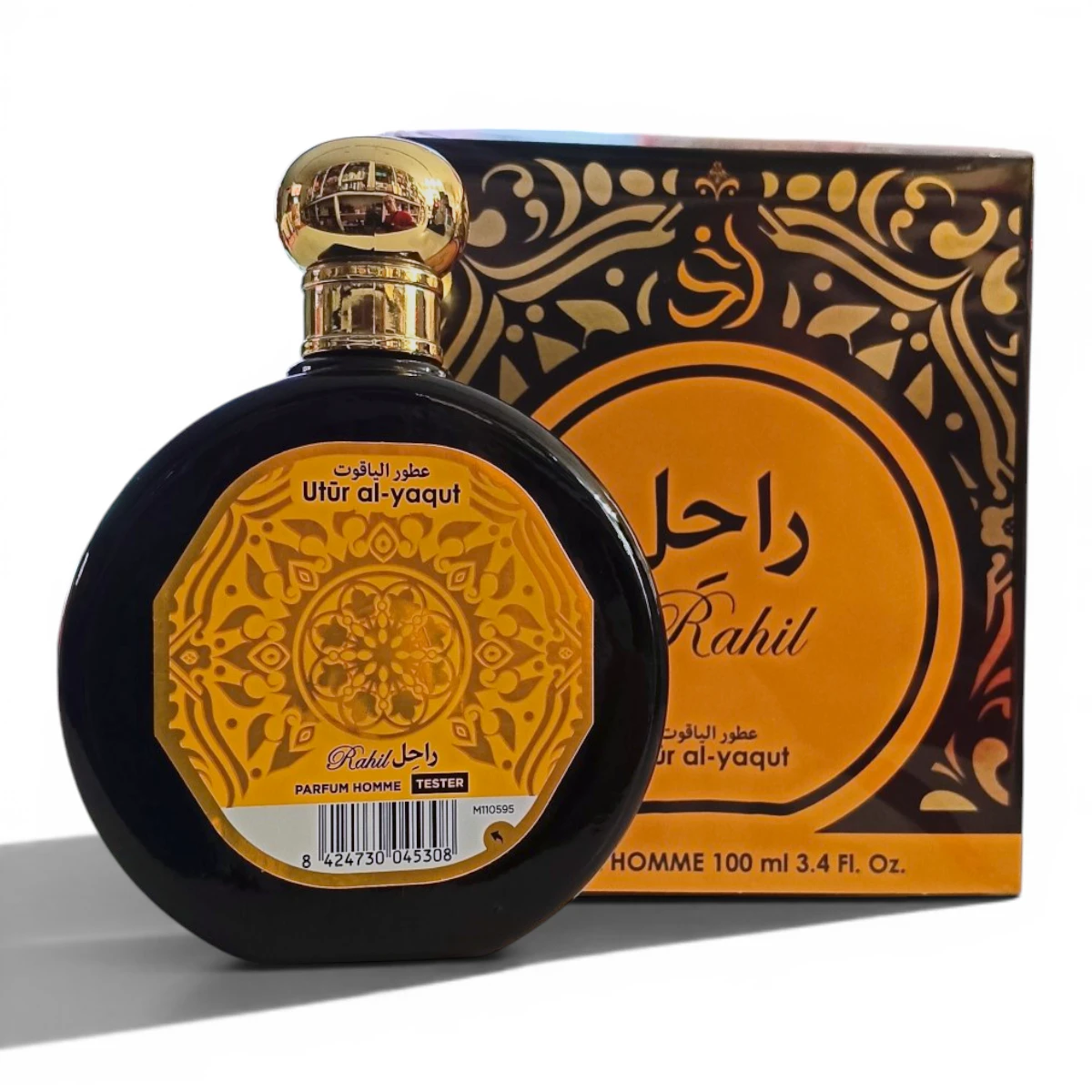 Un frasco redondo de perfume negro con tapón dorado está delante de su caja decorativa a juego. Ambos presentan intrincados motivos dorados y texto en árabe, con Rahil y Utūr al-yaqut escritos en el envase.