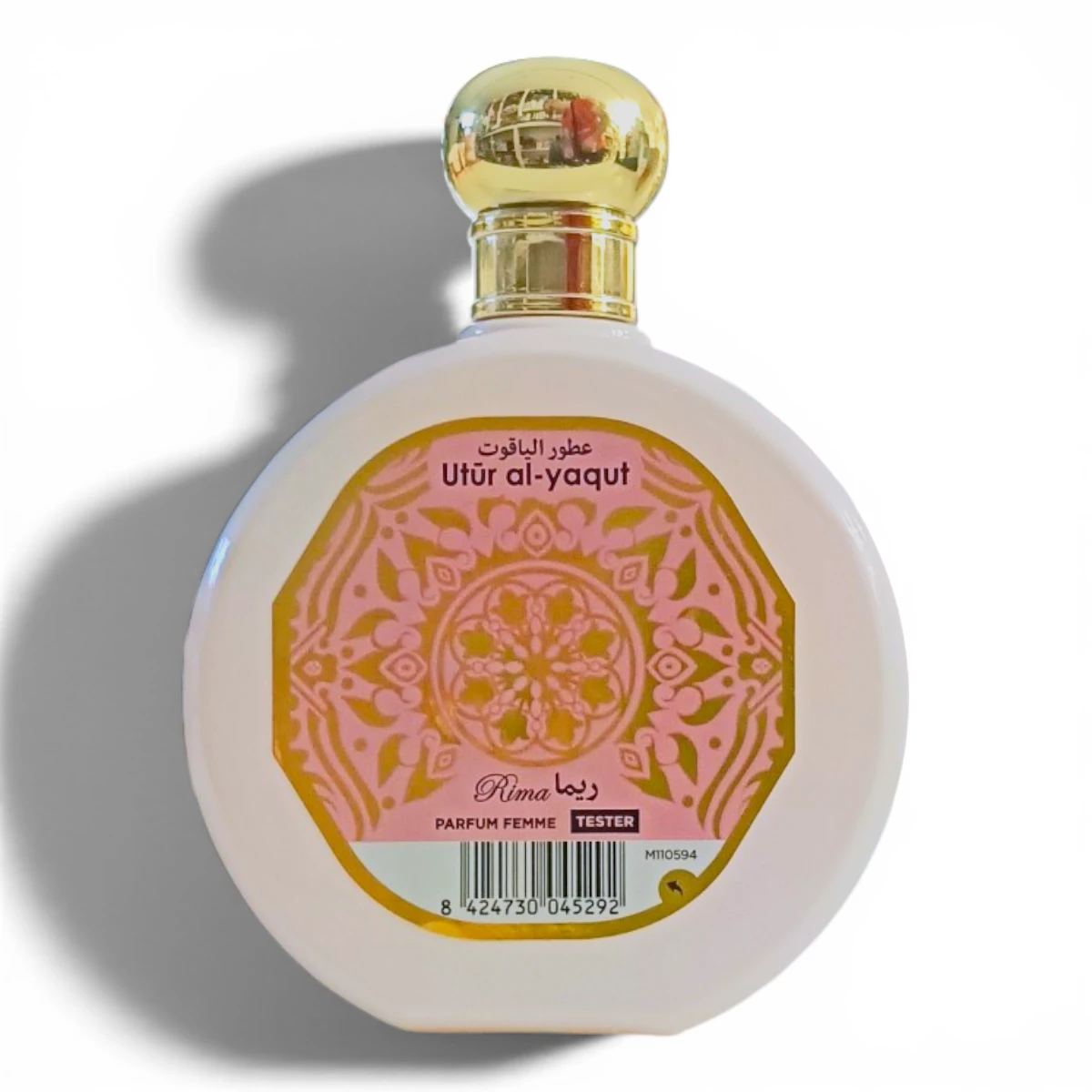 Frasco de perfume redondo con tapón dorado, con una etiqueta decorativa rosa y dorada en la que se lee Utur al-yaqut en árabe e inglés, y Rima con PARFUM FEMME y TESTER debajo.
