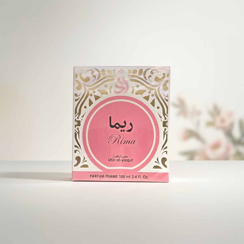 Caja de perfume etiquetada como Rima, con detalles decorativos dorados, texto en árabe e inglés y colores rosa y blanco. La caja está colocada sobre una superficie clara con un fondo floral difuminado.