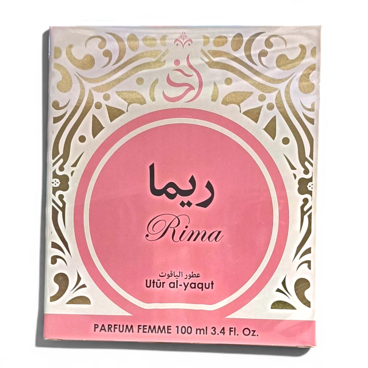 Caja de perfume rosa y dorada con la inscripción Rima en inglés y árabe, con motivos decorativos dorados en los laterales. En la caja también se lee Utūr al-yaqut y Parfum Femme 100 ml 3.4 Fl. Oz.