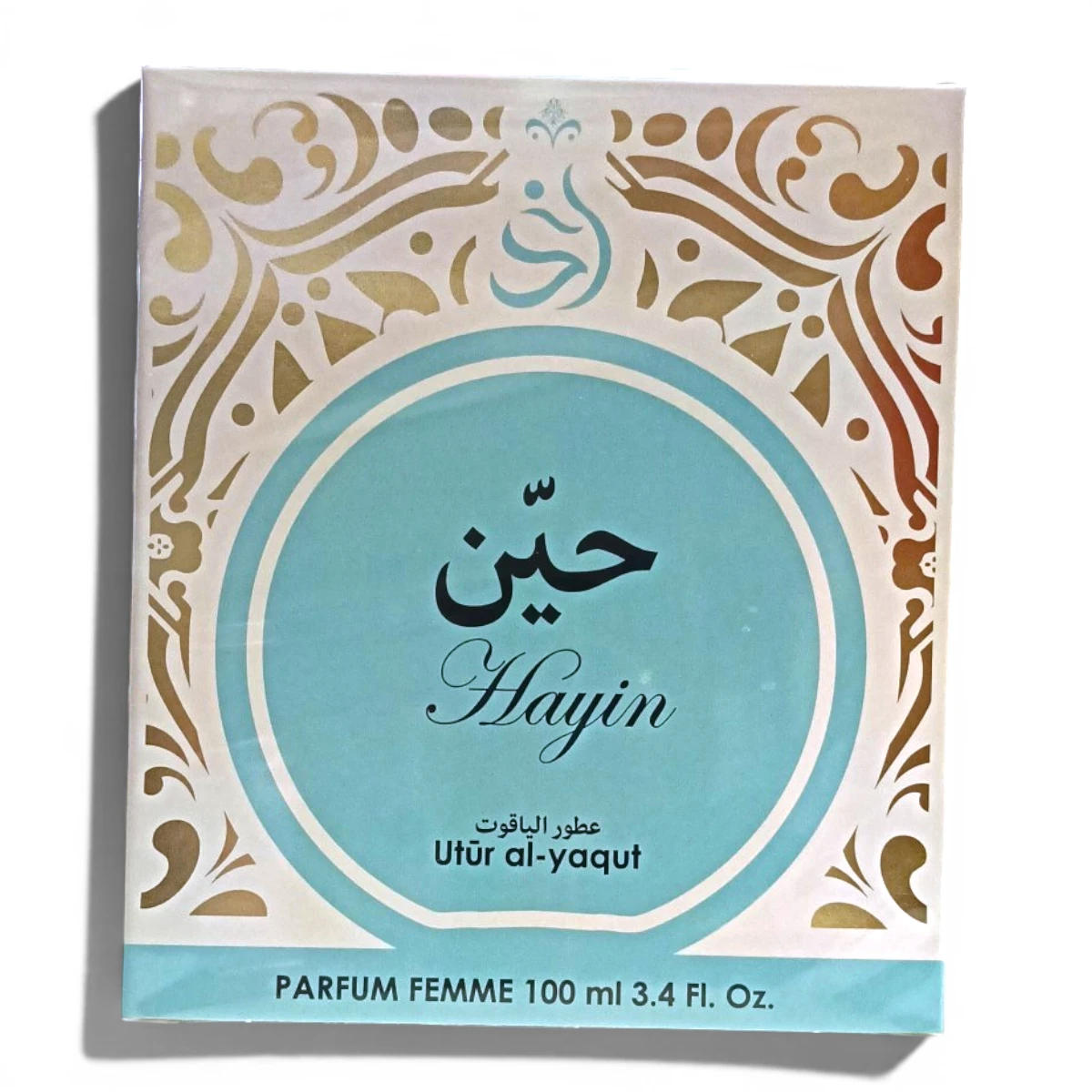 Caja de perfume con un diseño ornamentado en azul y dorado, con caligrafía árabe y el texto Hayin, Utūr al-yaqut, y PARFUM FEMME 100 ml 3.4 Fl. Oz. en la parte delantera.