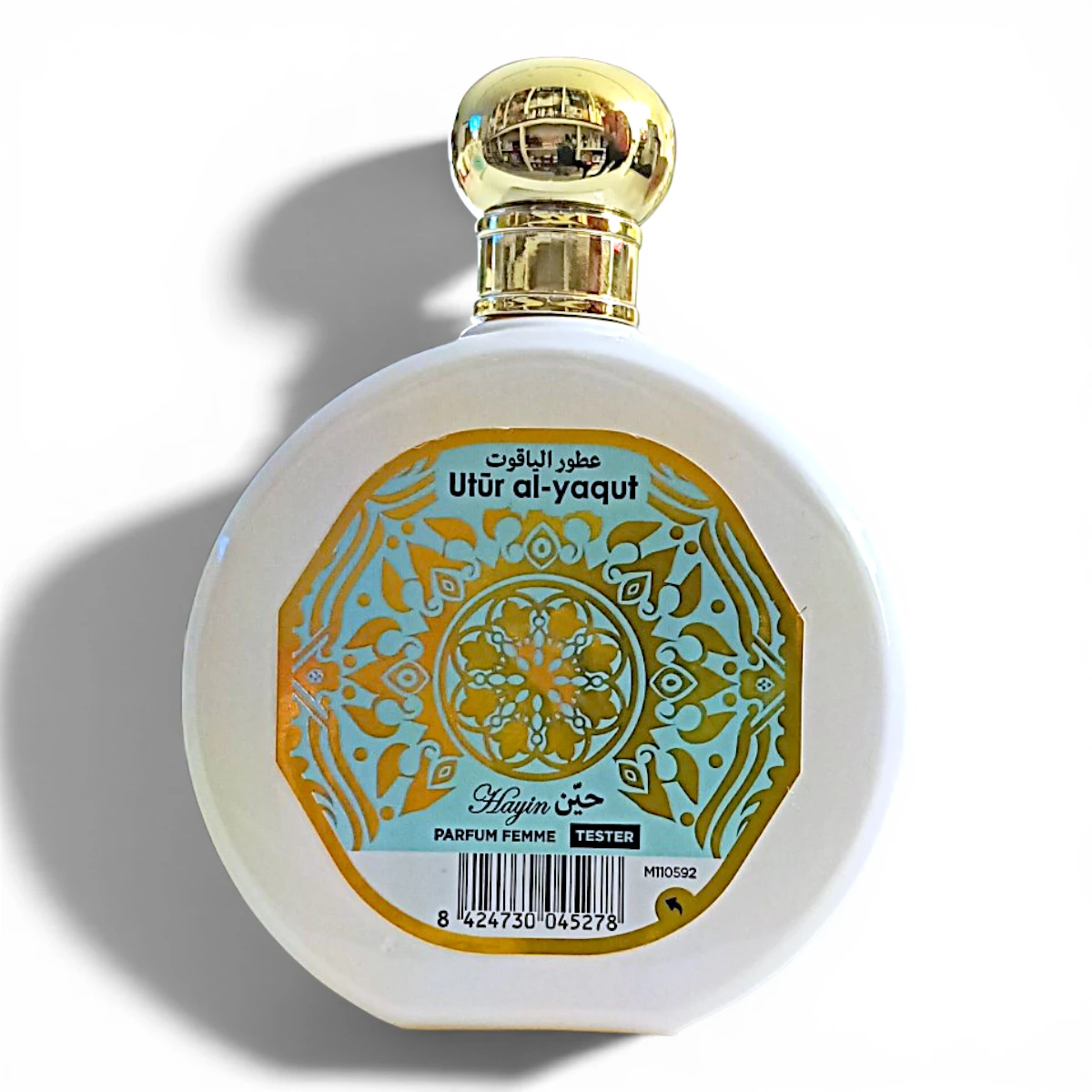 Frasco redondo de perfume blanco con tapón dorado y etiqueta decorativa dorada en la que se lee Utur al-yaqut en árabe e inglés, con Hajun Parfum Femme Tester debajo de un motivo floral.