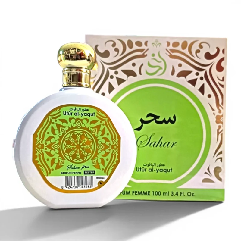 Un frasco de perfume blanco con tapón dorado y etiqueta verde ornamentada, etiquetado Sahar y Utûr al-yaqut, está delante de una caja decorativa verde y dorada a juego con diseños similares y escritura árabe.
