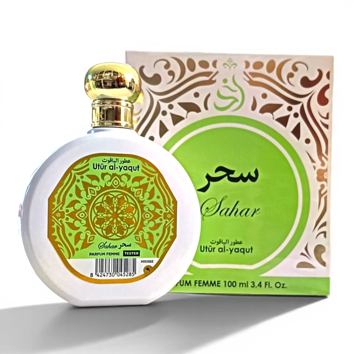 Un frasco de perfume blanco con tapón dorado y etiqueta verde ornamentada, etiquetado Sahar y Utûr al-yaqut, está delante de una caja decorativa verde y dorada a juego con diseños similares y escritura árabe.