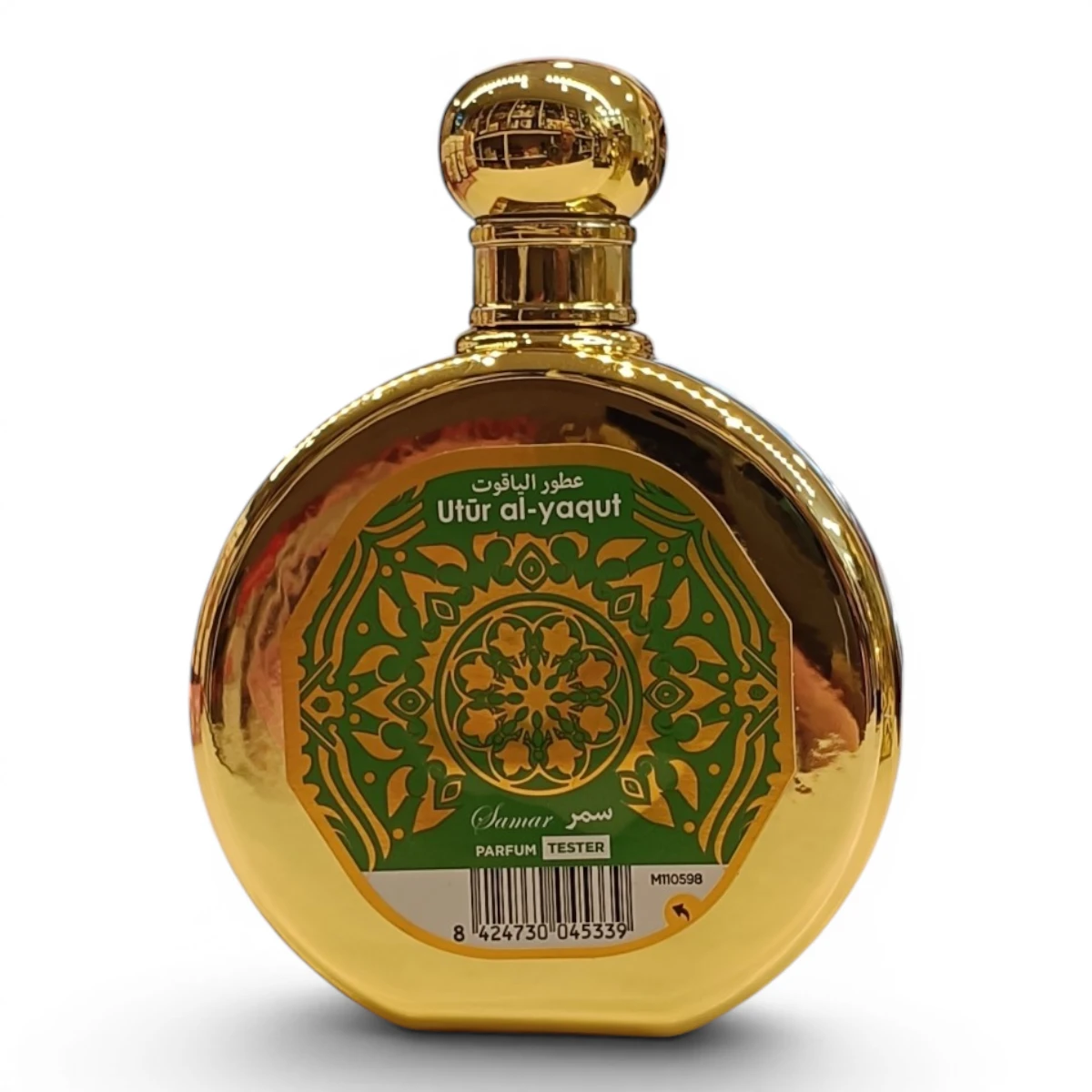 Frasco de perfume redondo, dorado, con una etiqueta de motivos florales verdes y dorados en la que se lee Utr al-yaqut en árabe e inglés, y Samar debajo. El frasco tiene un tapón redondo dorado y una etiqueta blanca de prueba en la parte inferior.