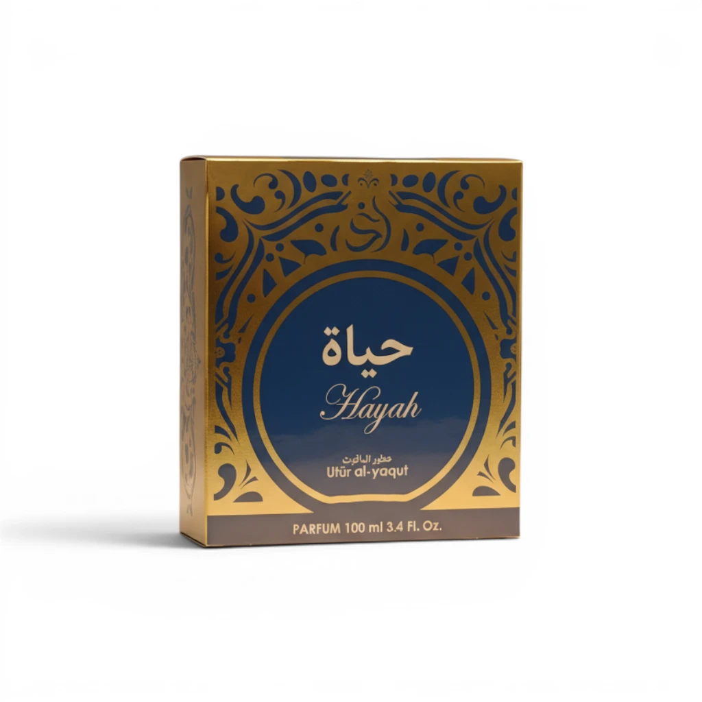 Caja dorada y azul de perfume Hayah, con escritura árabe y motivos ornamentales. El texto dice Hayah, Uthir al-yaqut, y PARFUM 100 ml 3.4 Fl. Oz. en el anverso.