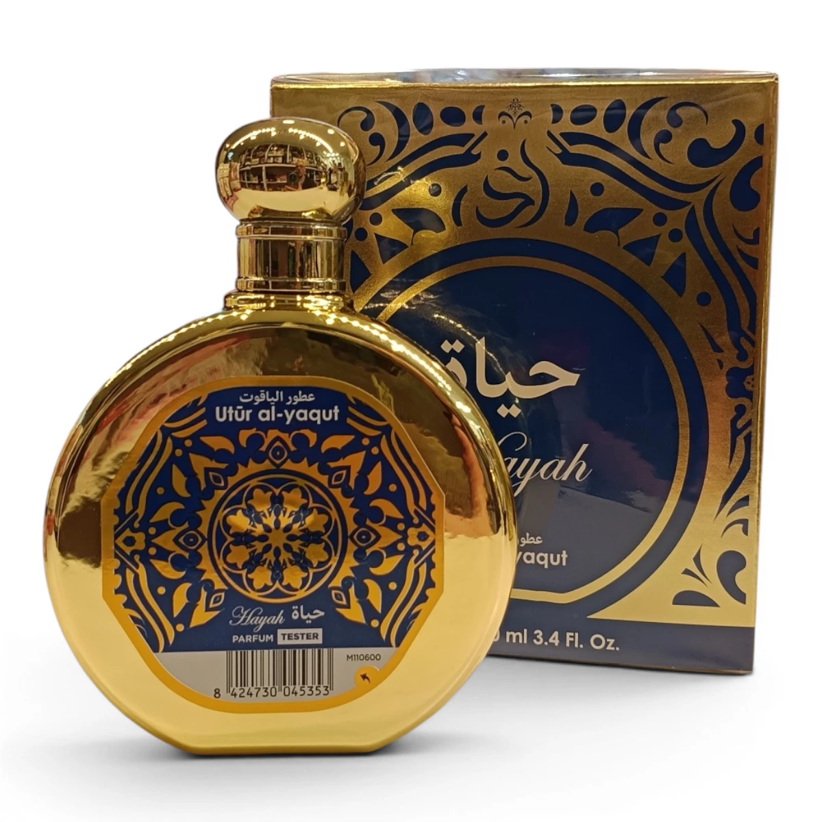 Un frasco redondo de perfume dorado, con la etiqueta Utur al-yaqut y motivos decorativos azules y dorados, delante de una caja azul y dorada a juego. El envase contiene textos en árabe e inglés.